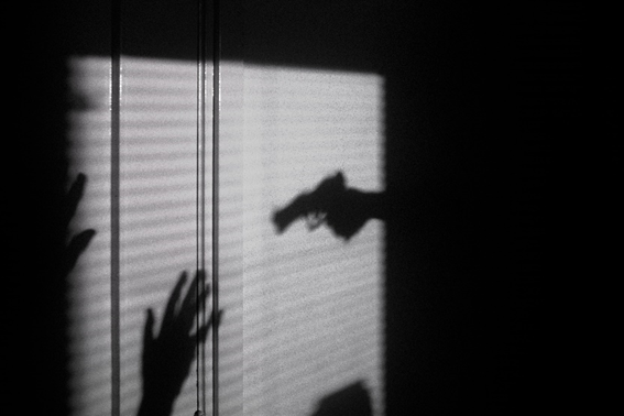 shadow of a hand holding a gun pointed at a person with their hands up