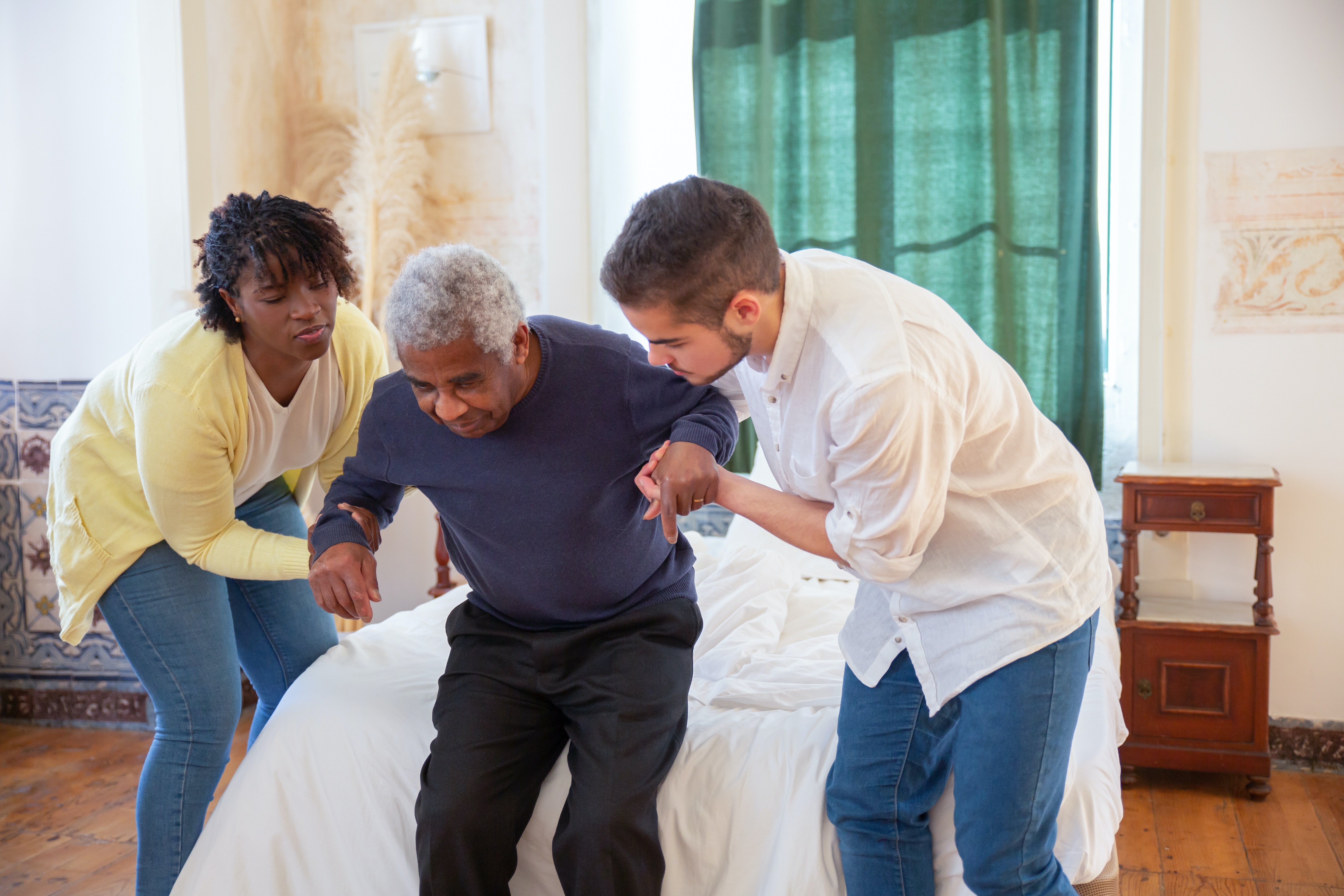 Two health care workers helping an elderly person stand up.