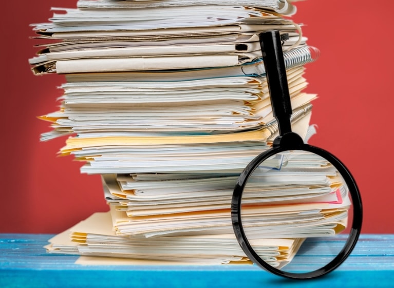 stack of folders and notebooks with a magnifying glass