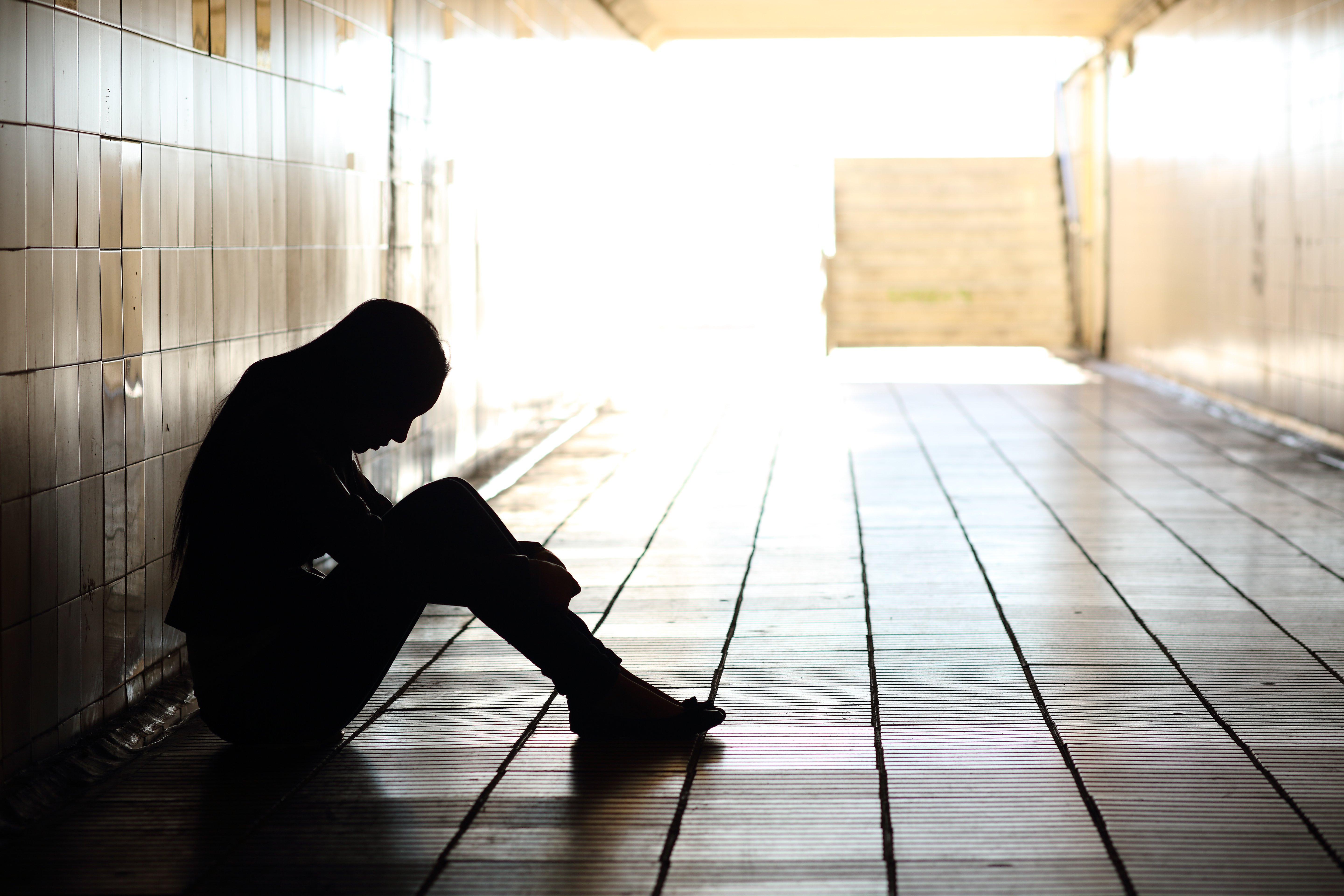 Sad teenager sitting against the wall in a school hallway