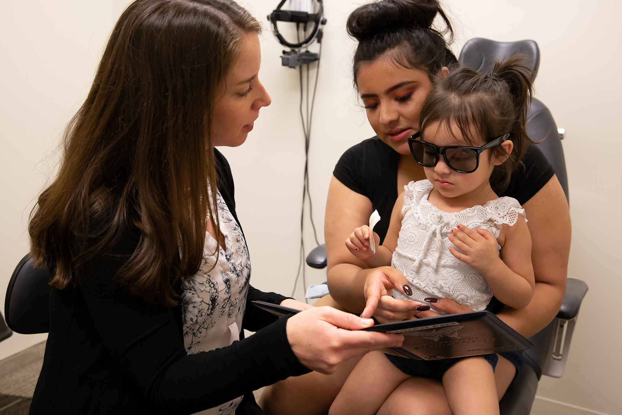 A health care worker talking with a woman and a toddler in an examination room.