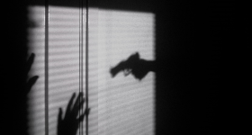 shadow of a hand holding a gun pointed at a person with their hands up