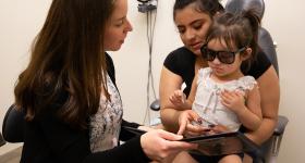 A health care worker talking with a woman and a toddler in an examination room.