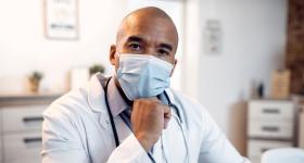 Male black doctor wearing a mask looking at the camera